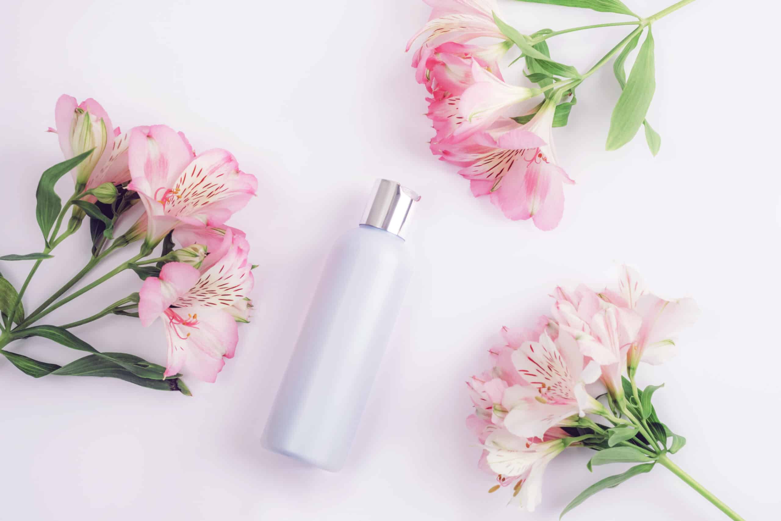 blue cosmetic bottle and alstroemeria pink flowers on white background, flat lay, top view. blank label for branding, mockup. natural organic eco cosmetics